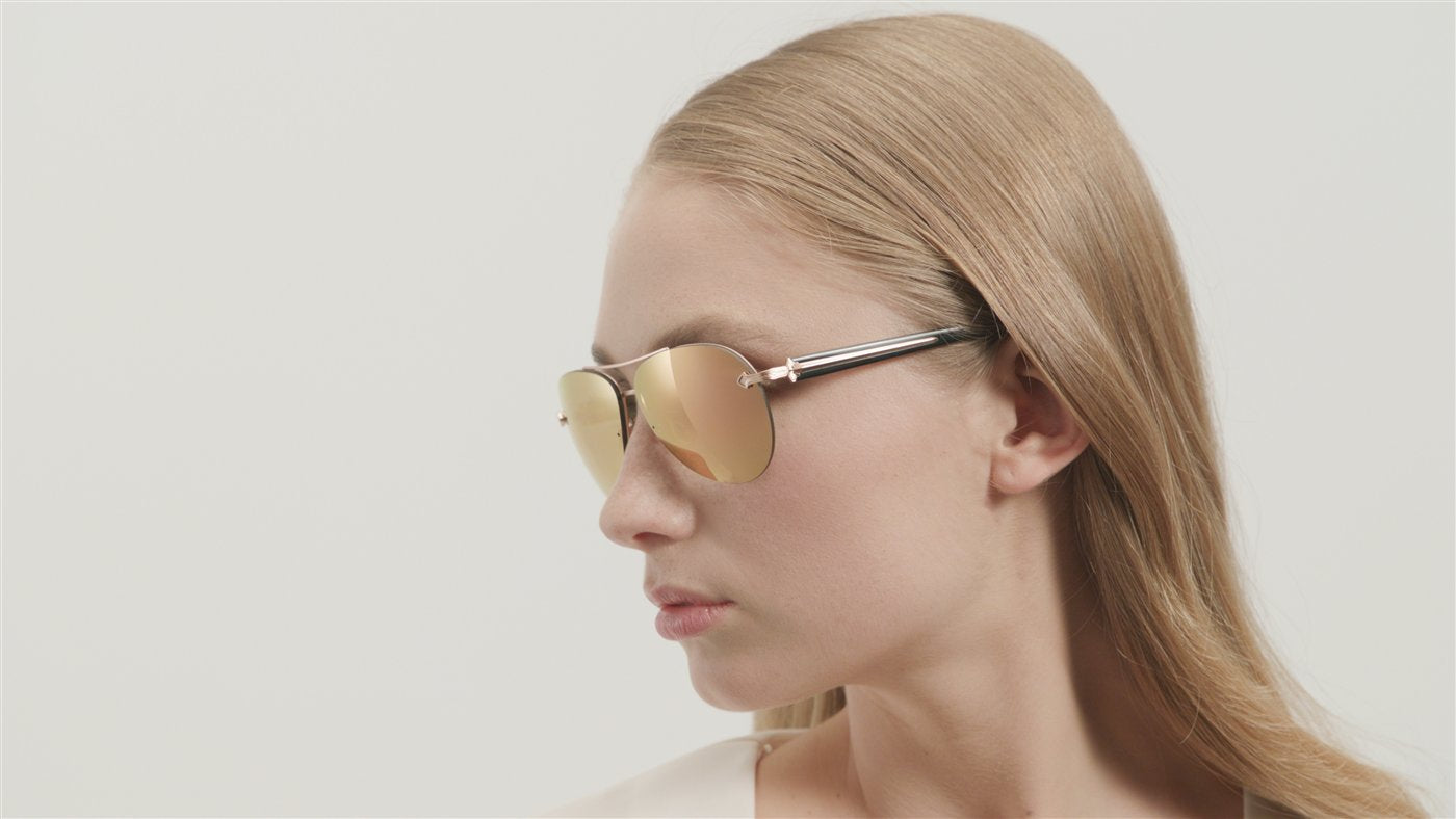 Editorial side profile of a person wearing gold-toned sunglasses against a neutral background.